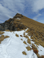 Looking up to a peak on a tussocky hill with a bit of snow on the lower parts