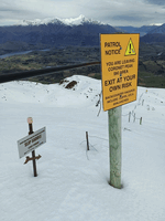 Two signs in snow, one for mountain bikers pointing down the hill saying 'SLIP SADDLE, steep terrain', the other saying 'You are leaving Coronet Peak ski area, exit at your own risk'