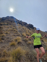 Soph running down a tussocky hill with the afternoon sun above the peak in the background