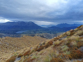 Slanting tussock hill with clouds and rain in the distance over moutains and lakes